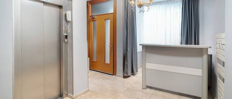 A hotel lobby with a reception desk, a wooden door, an elevator, and a chandelier.