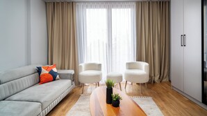 A modern living room with a grey sofa, two white armchairs, a wooden coffee table with a plant, and a large window with beige curtains. - Pia Global - Gümüşsuyu (İstanbul)