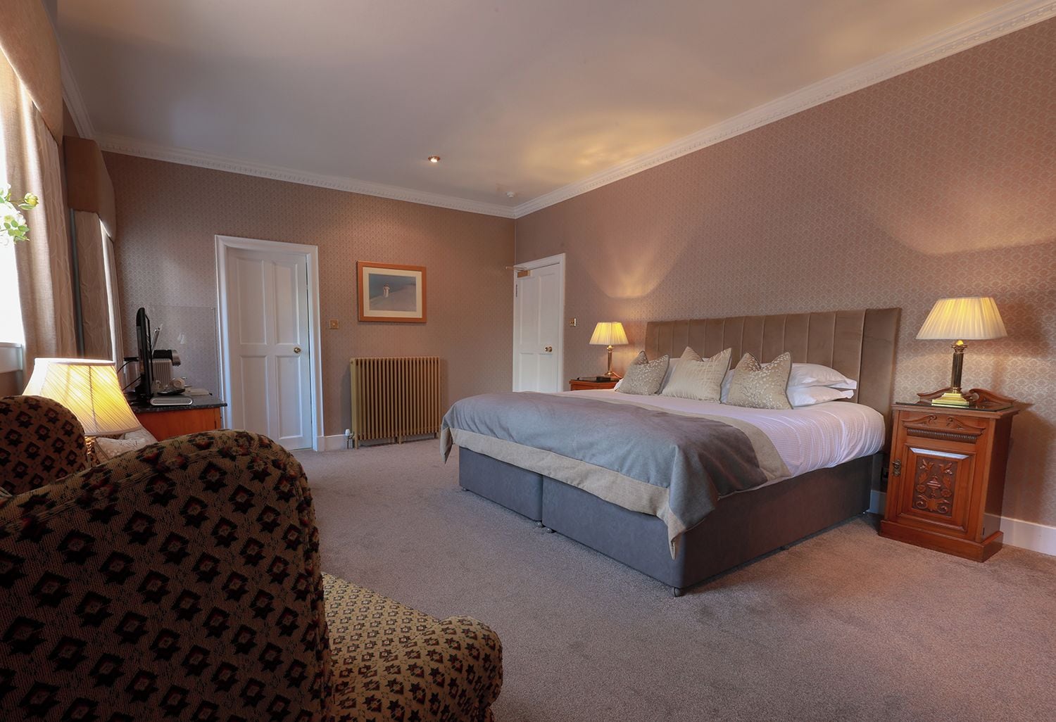 A hotel room with a large bed, two bedside tables, a chair, a radiator, and a picture on the wall.
