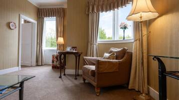 A room with a brown leather sofa, a small table with a lamp, and a window with curtains.