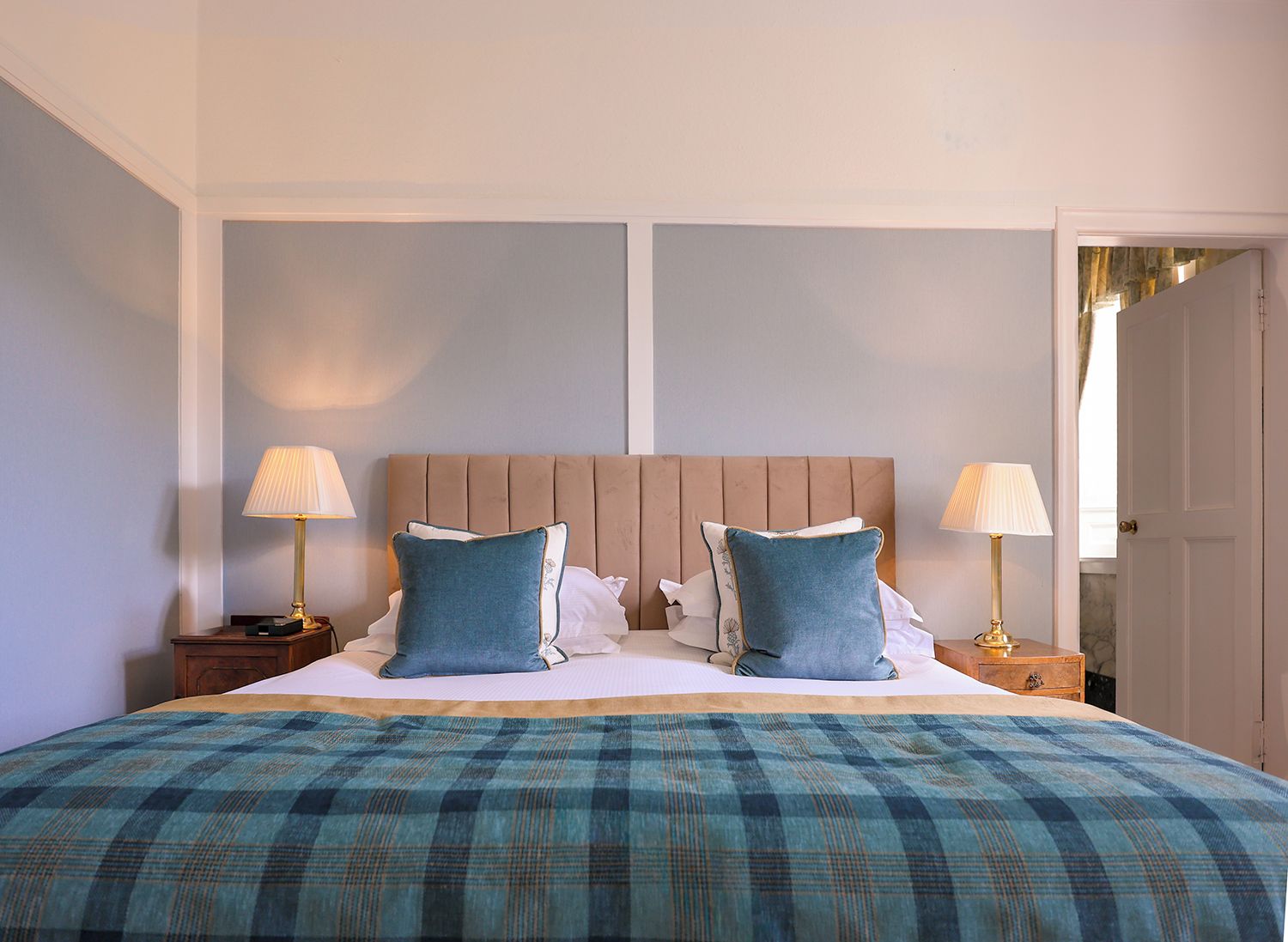 Habitación de hotel con una cama grande, dos mesitas de noche y una puerta que da a otra habitación.