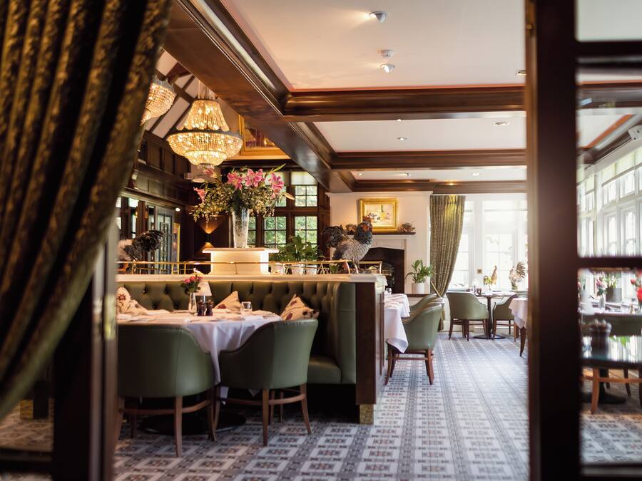 Un restaurante con zona de bar, asientos tapizados en verde, candelabros y suelo estampado.