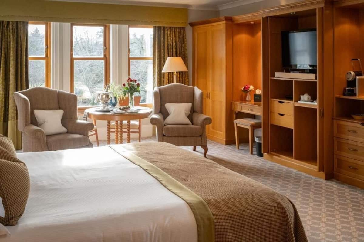 Ein Hotelzimmer mit einem Bett, zwei Sesseln, einem kleinen Tisch mit Lampe, einem Fernseher und einem Kleiderschrank.