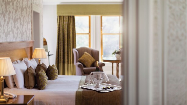 Une chambre d’hôtel avec un lit bien fait, une table de chevet avec une lampe, une chaise et une petite table sur laquelle se trouvent une bouteille et des verres.
