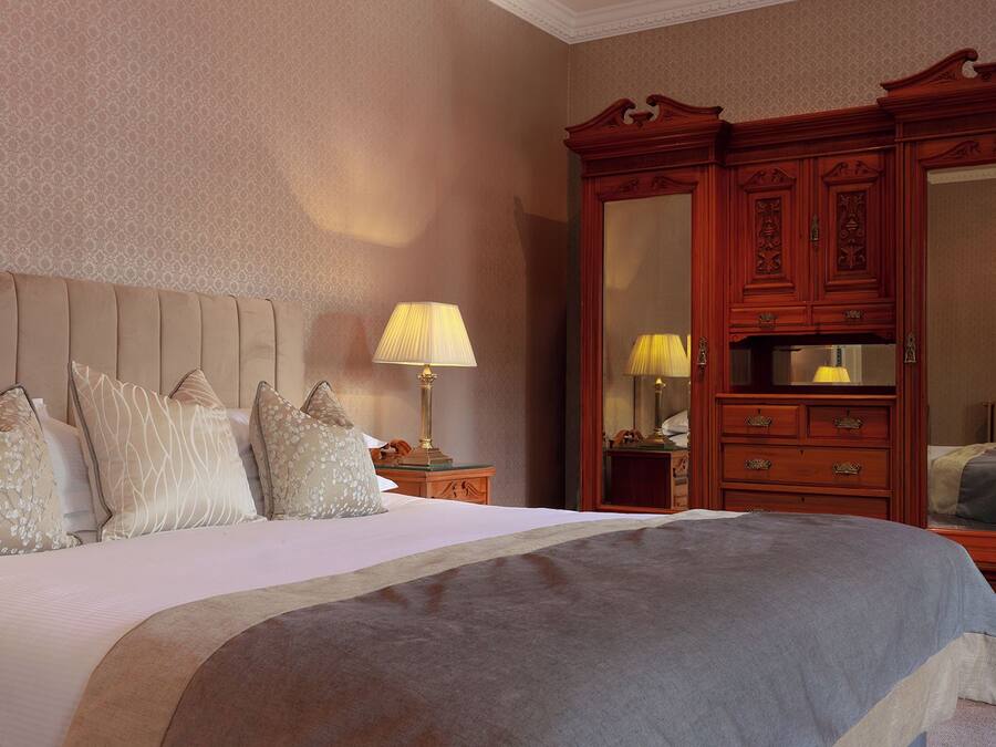 Una habitación de hotel con una cama grande, un armario de madera, una mesita de noche con lámpara y un espejo.
