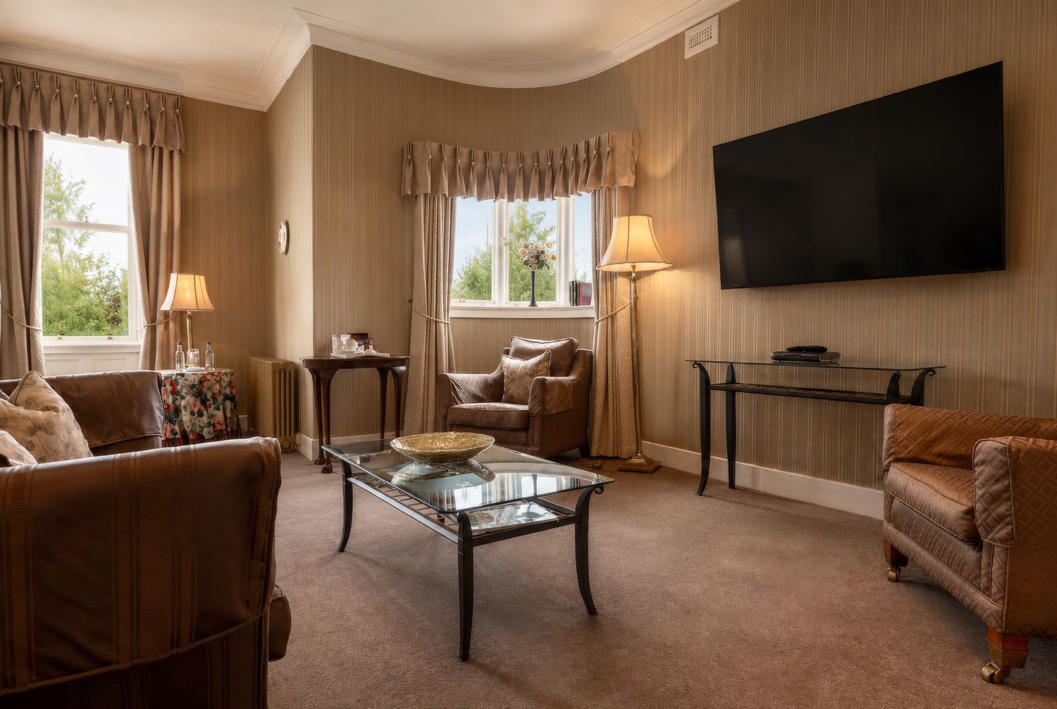 Een woonkamer met een bank, fauteuils, een glazen salontafel, een televisie en een lamp.