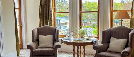 A room with two armchairs, a small round table, and large windows offering a view of the outdoors.