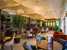 Ampla área de estar com poltronas de couro, um bar ao fundo e um candelabro.
