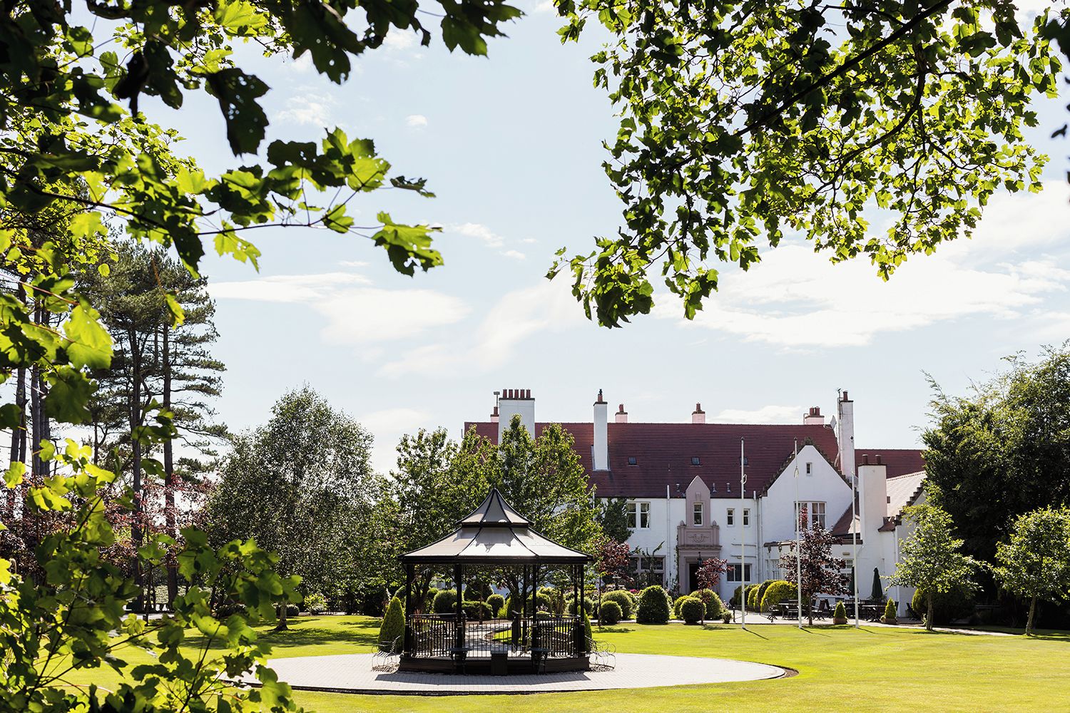 A gazebo in a well-maintained garden with a large building in the background.