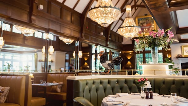 Un restaurant avec de hauts plafonds, des lustres et des banquettes recouvertes d’un tissu vert.