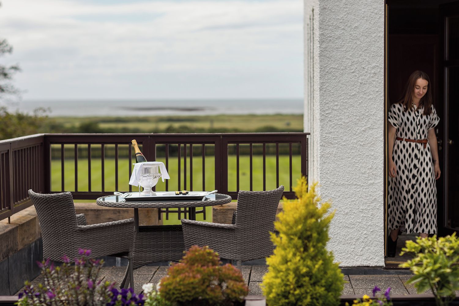 A balcony with wicker furniture, a bottle of champagne, and a view of the countryside.