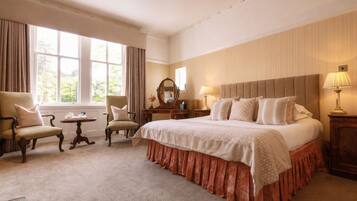 Habitación de hotel con una cama grande, dos sillones, una mesita, un aparador y una ventana con cortinas.