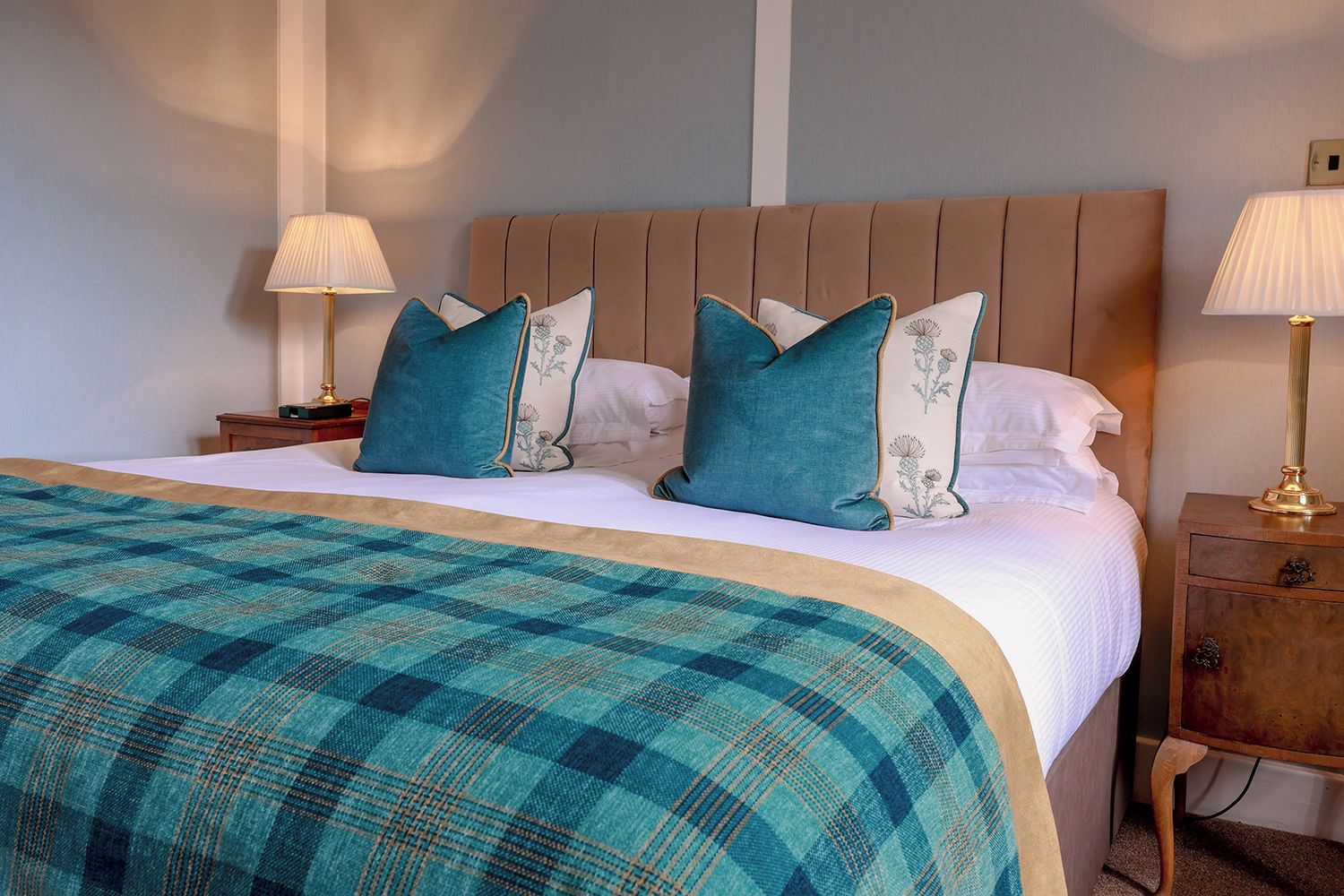 A neatly made bed with a plaid bedspread, two bedside tables with lamps, and a headboard.