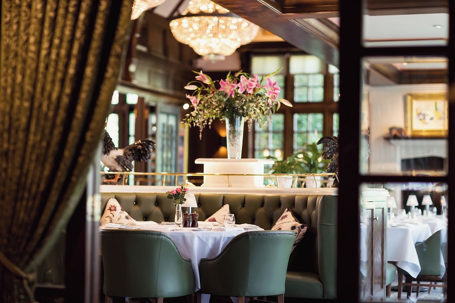 A restaurant interior with a booth seating arrangement, a chandelier, and a vase with flowers on the table.