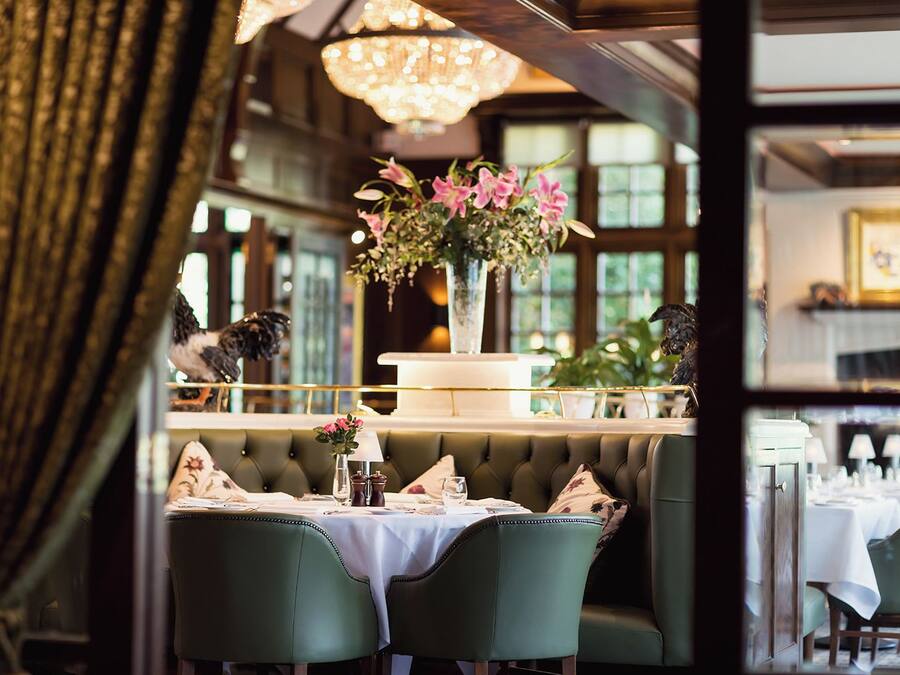 A restaurant interior with a booth seating arrangement, a chandelier, and a vase with flowers on the table.