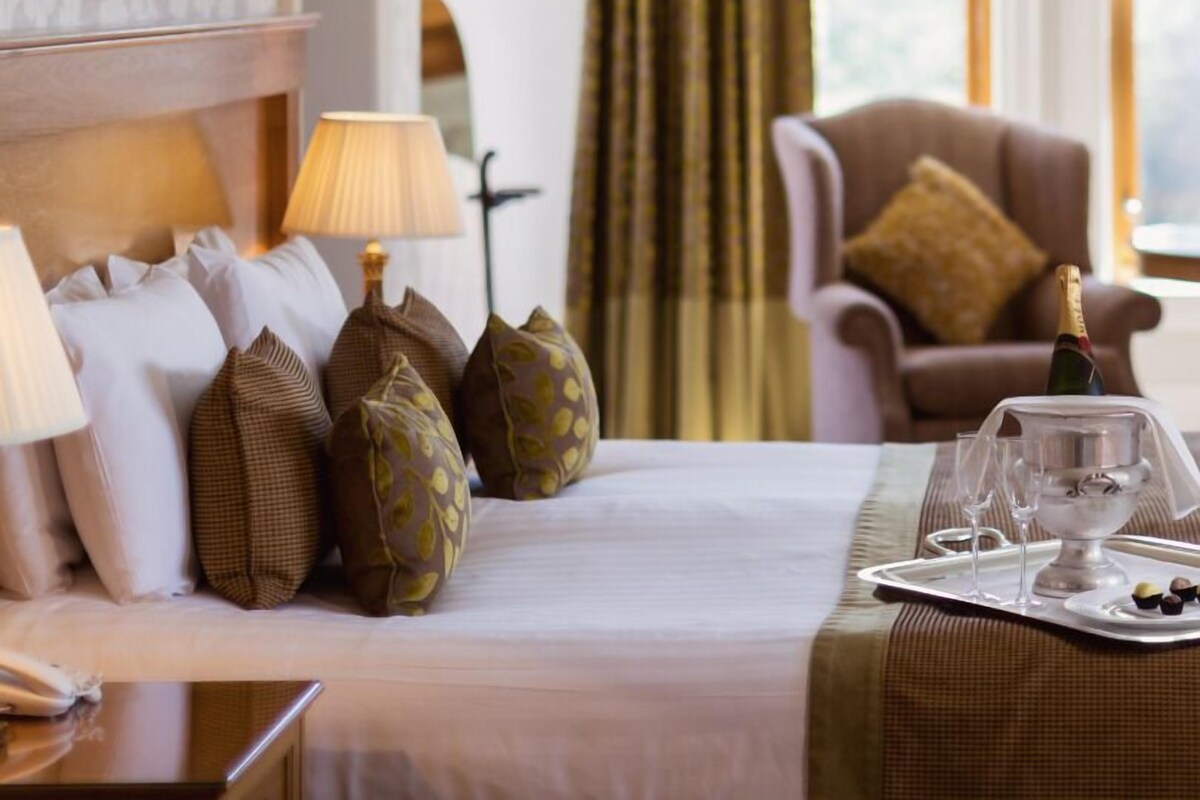 Habitación de hotel con una cama bien hecha, una silla, una mesa con una bandeja de vasos y aperitivos, y vistas al exterior a través de la ventana.