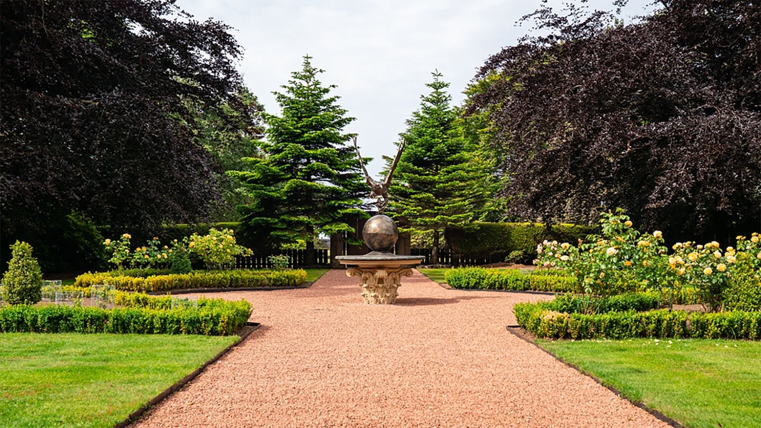 A garden pathway leading to a central fountain with a spherical ornament.
