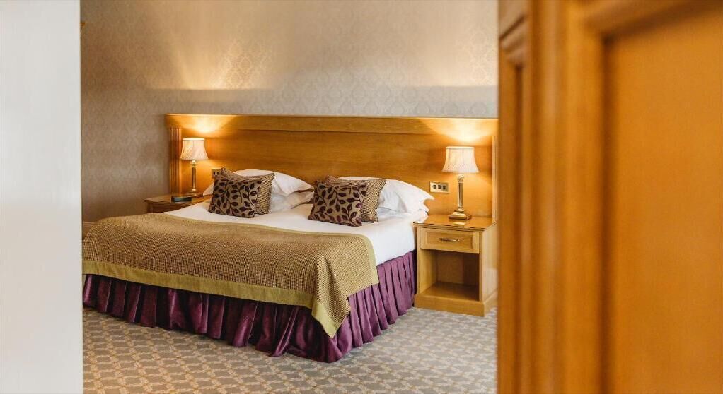 Una habitación de hotel con una cama grande, dos mesitas de noche y un cabecero de madera.