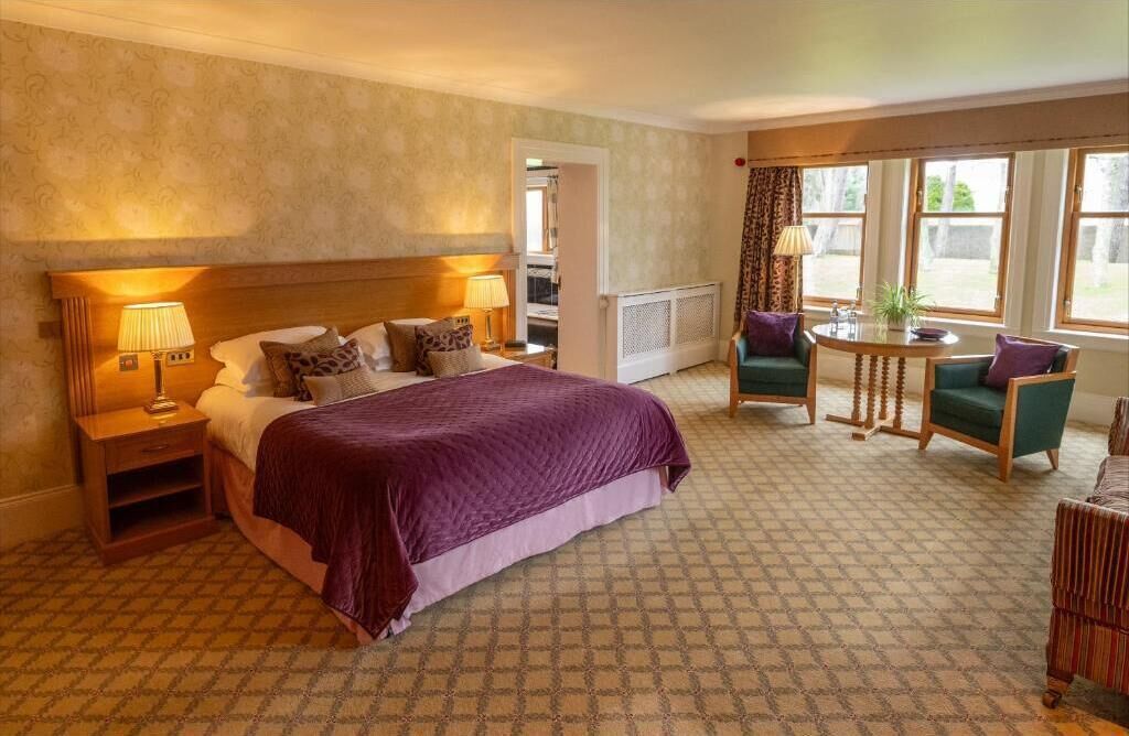 Ein Hotelzimmer mit einem großen Bett, einer Sitzecke mit Tisch und Stühlen sowie Blick durch das Fenster.