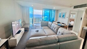 A modern hotel room with a large sofa, a flat-screen TV, a dining area, and a balcony with a view of the sea. - 5-star, 2 bdrm apt with the perfect view of Surfers Paradise beach (Surfers Paradise)