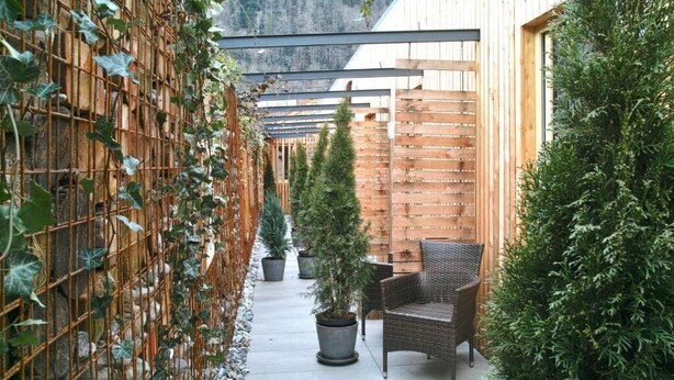A covered outdoor patio with a wooden fence, potted plants, and a wicker chair. - s'Matt BOB (Feldkirch)
