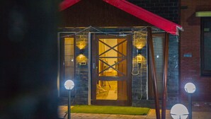 A building with a red roof, a wooden door with a cross pattern, and two wall-mounted lights.
