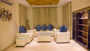 A modern living room with white sofas, a glass coffee table, and decorative pillows.