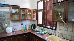 A kitchen with wooden cabinets, a countertop with various items, and a window with blinds.