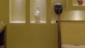 A room with a bed, a chair, and a wall with multiple display cases containing various sculptures.