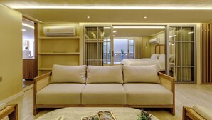 A modern living room with a beige sofa, a coffee table with magazines, and a large window with curtains.