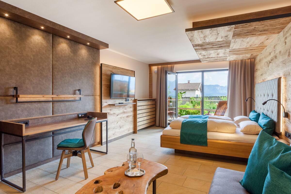 Een moderne hotelkamer met een houten bureau, een comfortabele bank, een bed met uitzicht en een balkon.