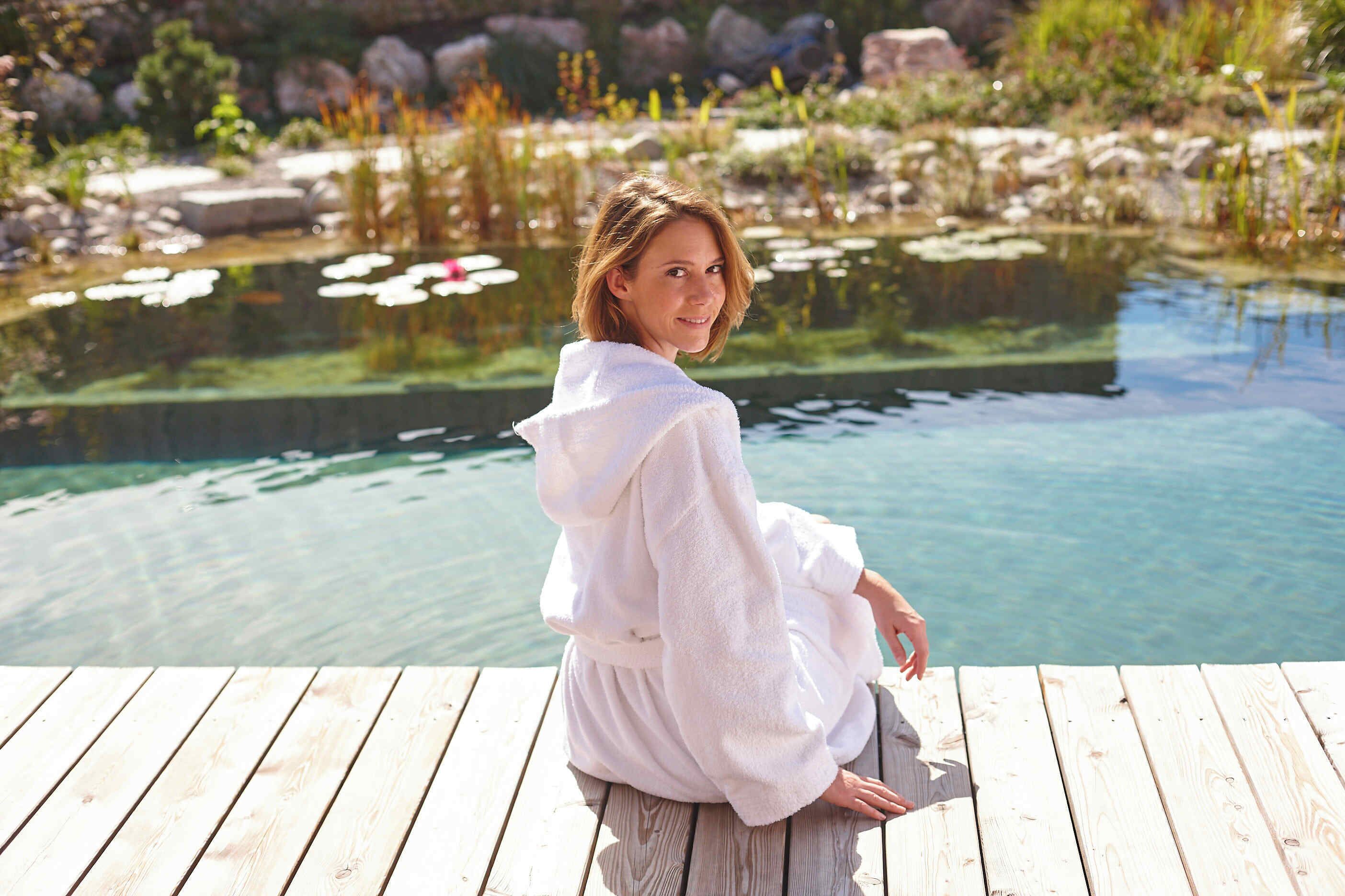 A person sitting on a wooden dock by a clear pond with lily pads.