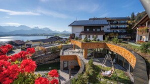 A modern resort with a glass-walled infinity pool, a wooden deck, and a view of a lake and mountains. - Biohotel Eggensberger (Fuessen)