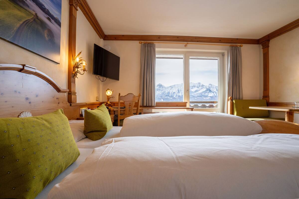 Hotelkamer met een groot bed, een bureau, een stoel, een televisie en een raam met uitzicht op de bergen.