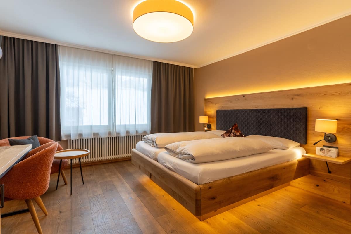 Een hotelkamer met een houten bed, een bureau, een stoel en een groot raam met gordijnen.