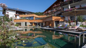 A pool area with lounge chairs, a stone pathway, and a building with balconies. - Biohotel Eggensberger (Fuessen)