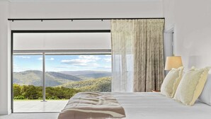 Un dormitorio con una cama grande, vistas a un paisaje montañoso y una puerta corrediza de vidrio.