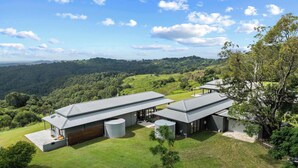 A modern house with a large lawn, two garage doors, and a view of a forested hill. - Panorama Farm - 3BD Wilderness Retreat (Hinterland Region)
