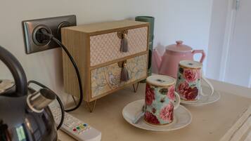 Een kitchenette met een waterkoker, een afstandsbediening, een houten kastje met decoratieve panelen en bloemendecor cups op een dienblad.