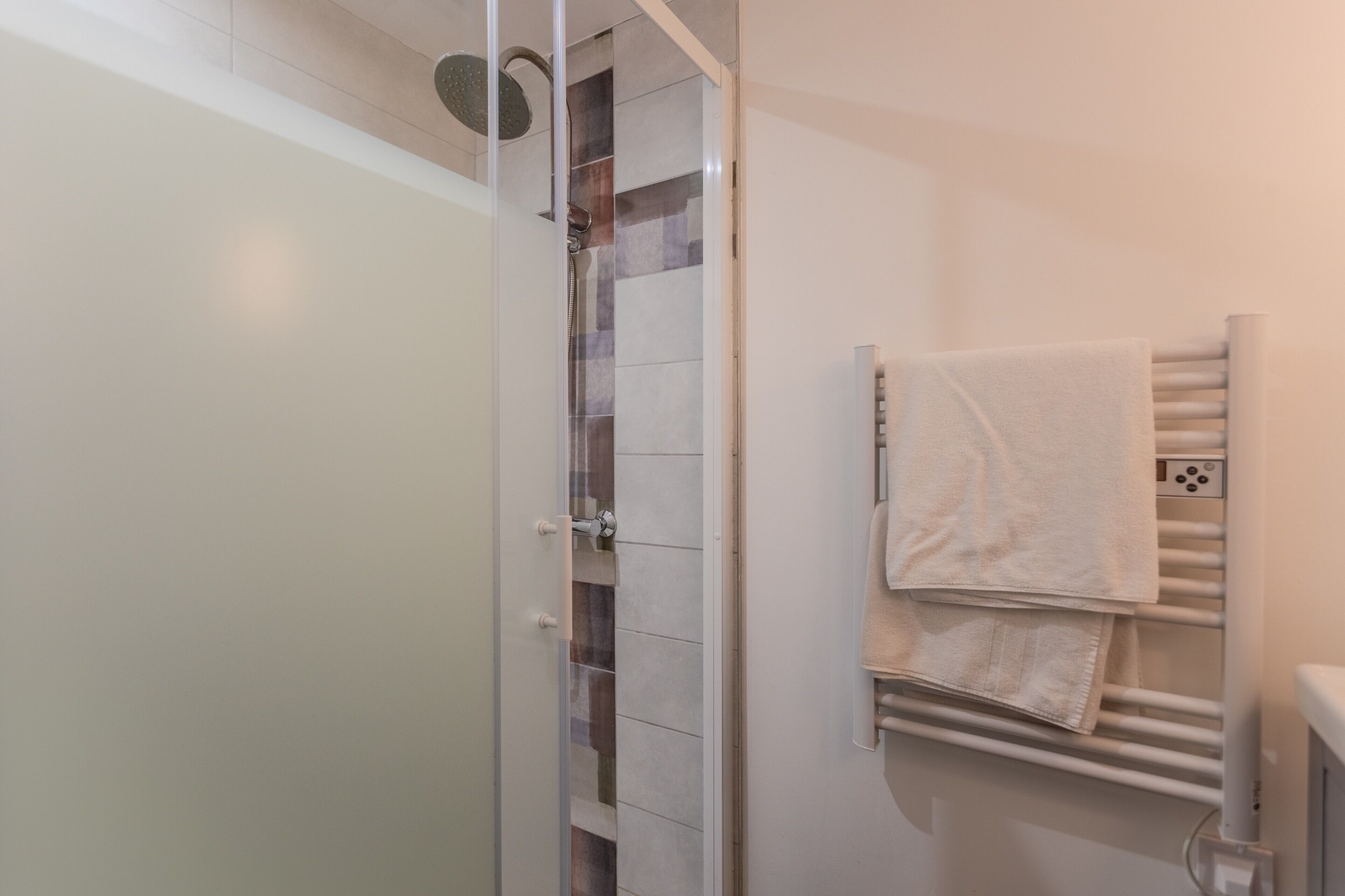 Een badkamer met een glazen douchecabine, een handdoekrek met handdoeken en een witte betegelde wand.