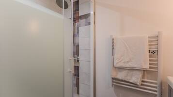 Een badkamer met een glazen douchecabine, een handdoekrek met handdoeken en een witte betegelde wand.
