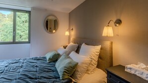 Une chambre à coucher avec un lit, des oreillers, une table de chevet, une lampe et une fenêtre.