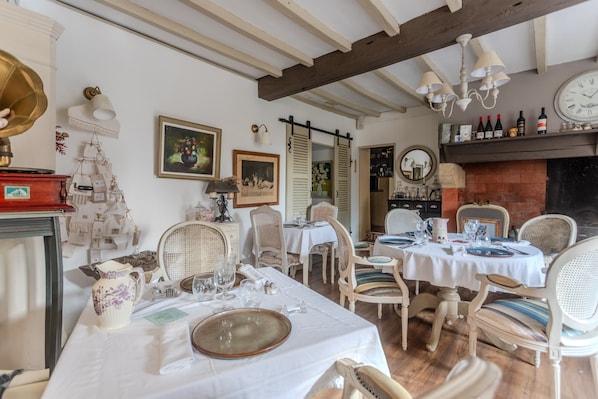 A dining area with tables set for four, wicker chairs, a fireplace, and a clock on the wall.