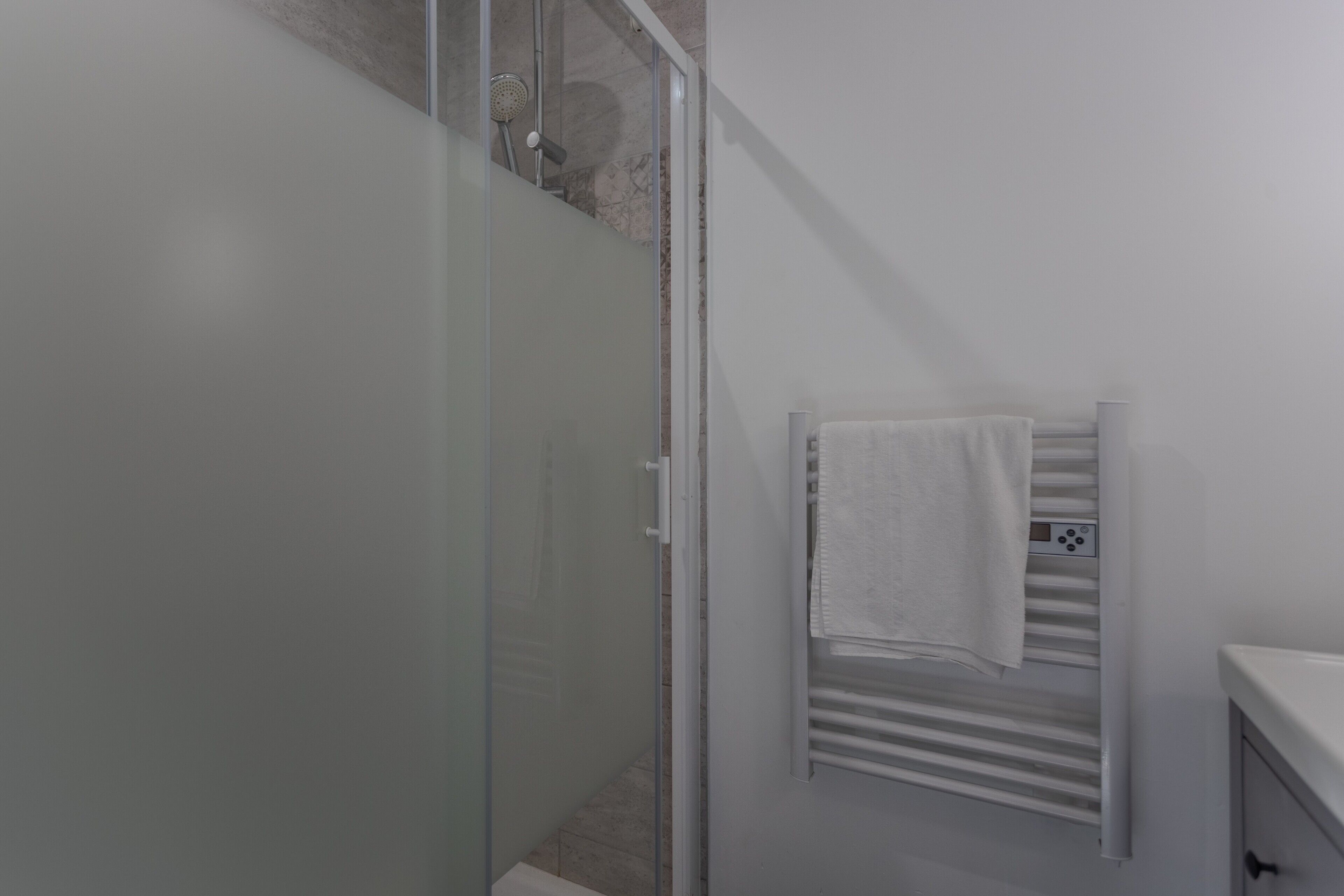 Un baño moderno con mampara de ducha de vidrio, toallero blanco y lavamanos blanco.