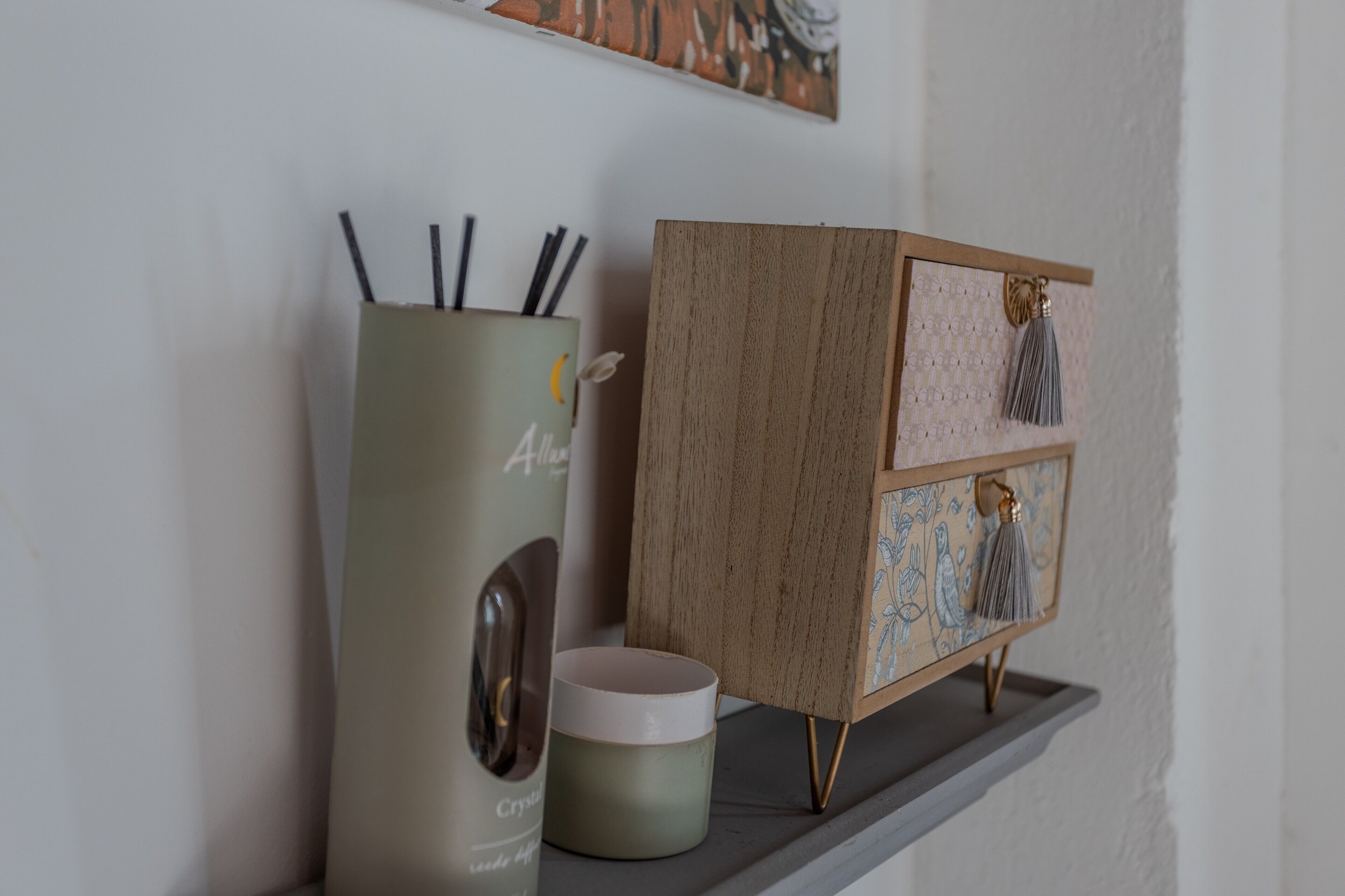 A shelf with a tall container, a smaller container, and a wooden cabinet with decorative elements.