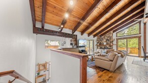 A spacious living area with a wooden ceiling, a stone fireplace, a large window, and a cozy seating area. - Evergreen Hideout Retreat (Kings Beach)