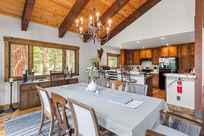 Una cocina amplia con armarios de madera, un comedor con una mesa grande y sillas, y una araña.