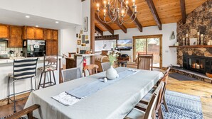 A spacious living area with a dining table, wooden chairs, a chandelier, a fireplace, and a kitchen in the background. - Evergreen Hideout Retreat (Kings Beach)