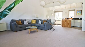A spacious living area with a grey sectional sofa, a coffee table, and a kitchen area in the background.