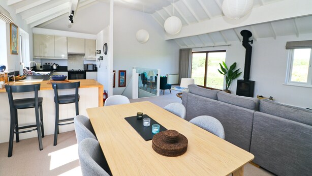 A modern kitchen with a dining area, a grey sofa, and a wooden table.